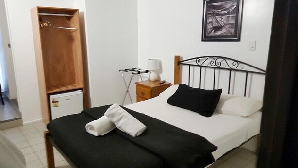 Un lit bien fait, avec un oreiller noir et blanc, une table de chevet avec une lampe et une armoire en bois.