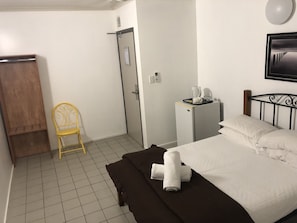A hotel room with a bed, a small desk with a coffee maker, a chair, and a wardrobe.