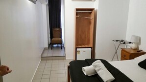 Une chambre d’hôtel comprenant un lit, un petit bureau avec une lampe, une chaise, une armoire et une porte donnant sur un balcon.