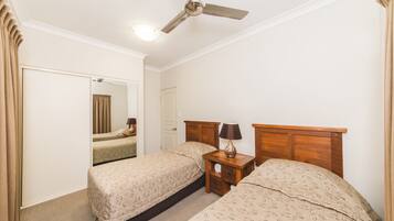 A hotel room with two single beds, a wooden headboard, a nightstand with a lamp, a ceiling fan, and a mirror on the wall.
