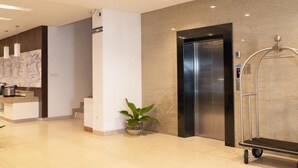 Een moderne lobby met een receptiebalie, een trap, een lift en een kamerplant.