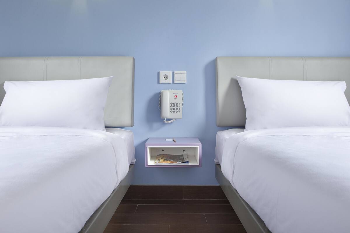 Quarto de hotel com duas camas, uma mesa de cabeceira com telefone e luminárias fixadas na parede.