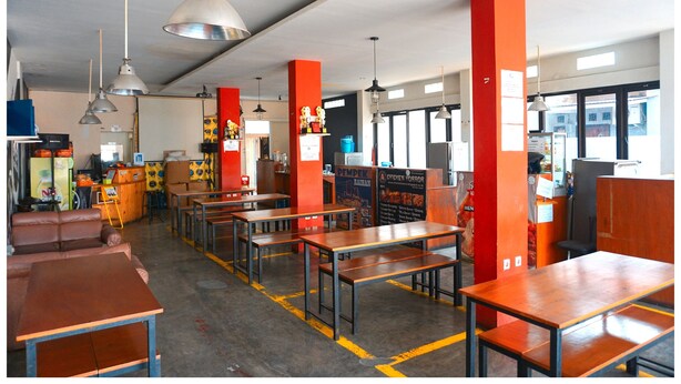 A restaurant with booths and tables, red pillars, and hanging lights. - Budi House & Food Station (Cimahi)