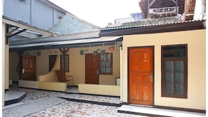A building with numbered doors, a tiled courtyard, and a covered area with a chair. - Budi House & Food Station (Cimahi)