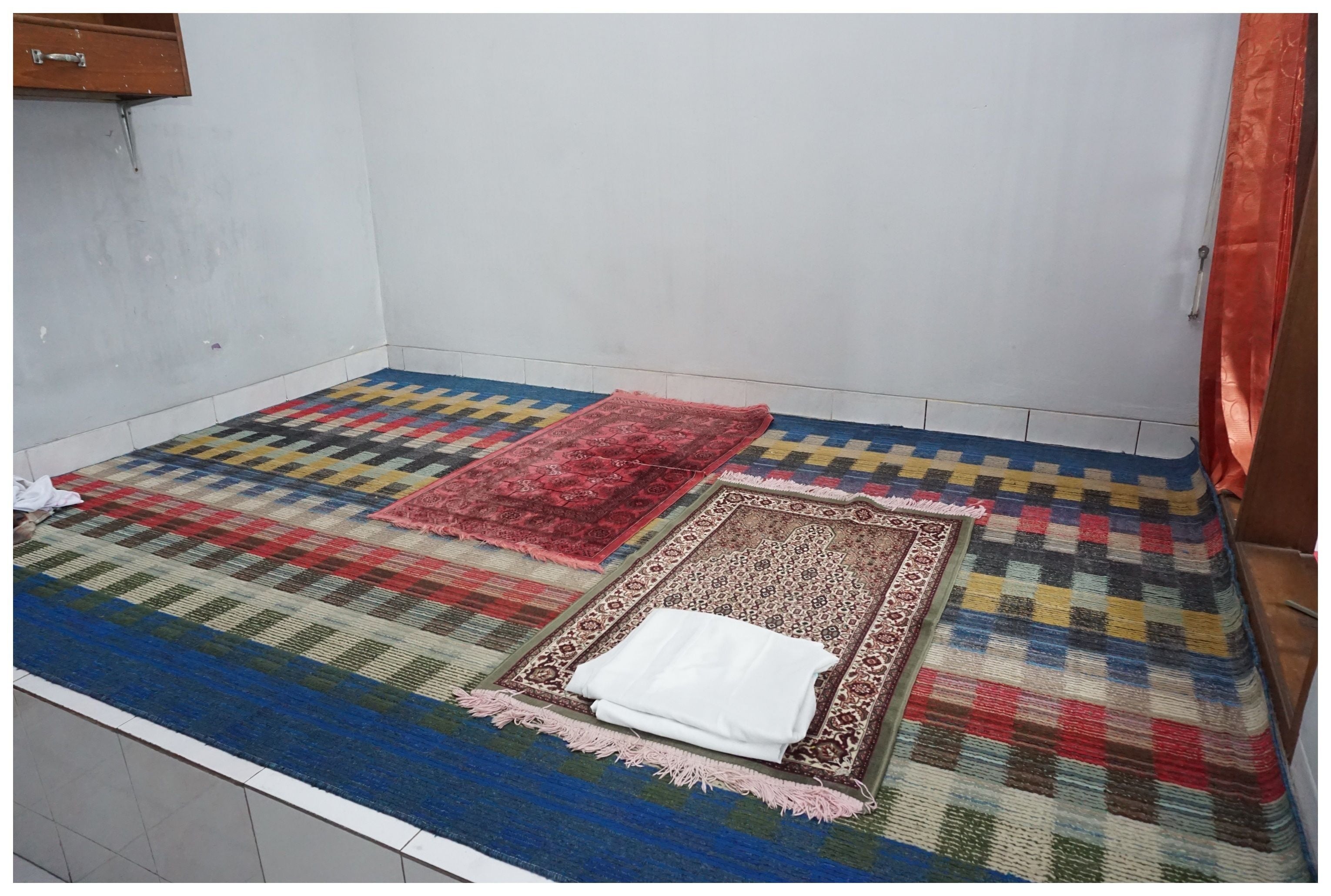 A room with a large, colorful area rug, a smaller patterned rug, and a white cloth on a matching rug.