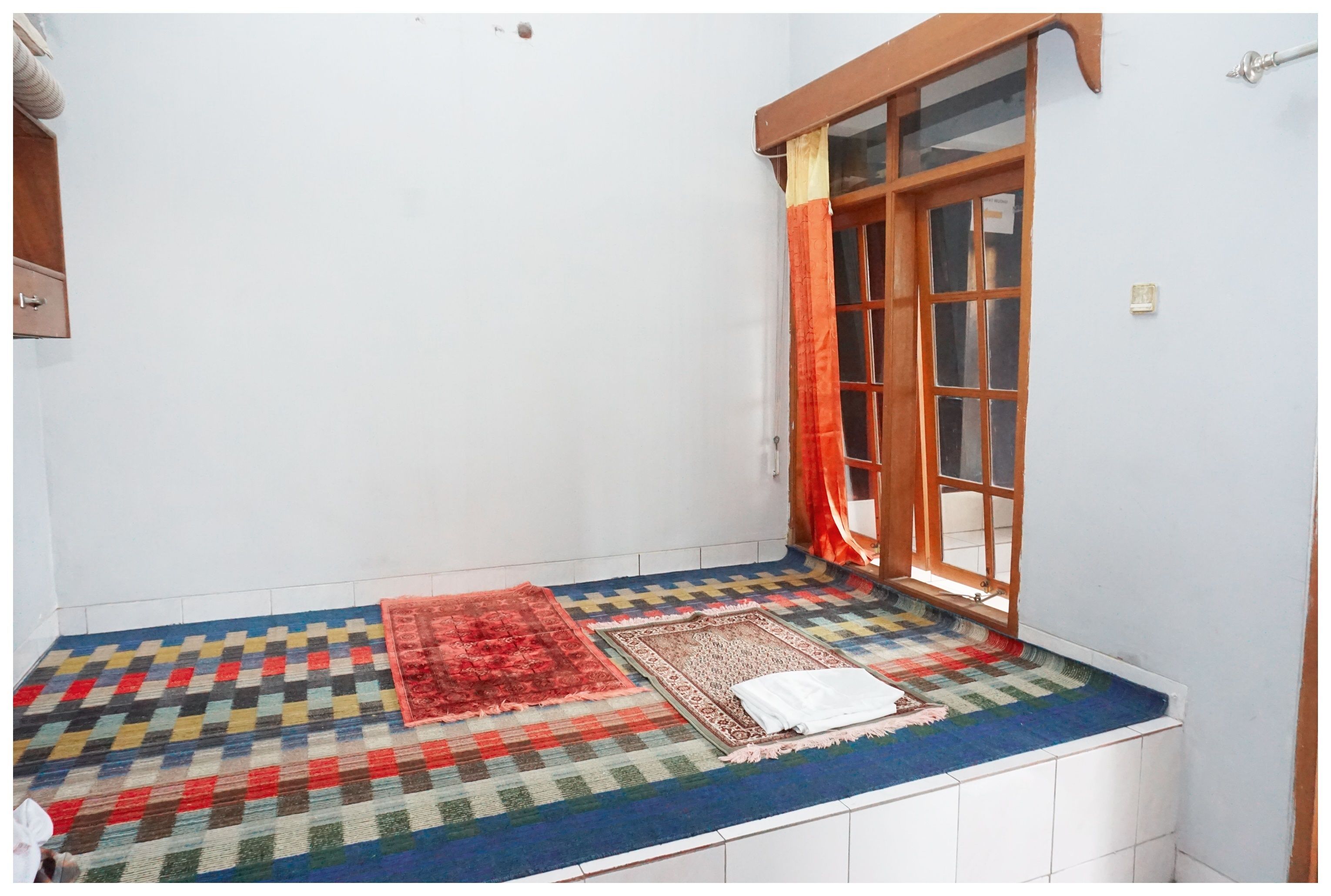 A small room with a window, a colorful mat, and a white towel on the floor.