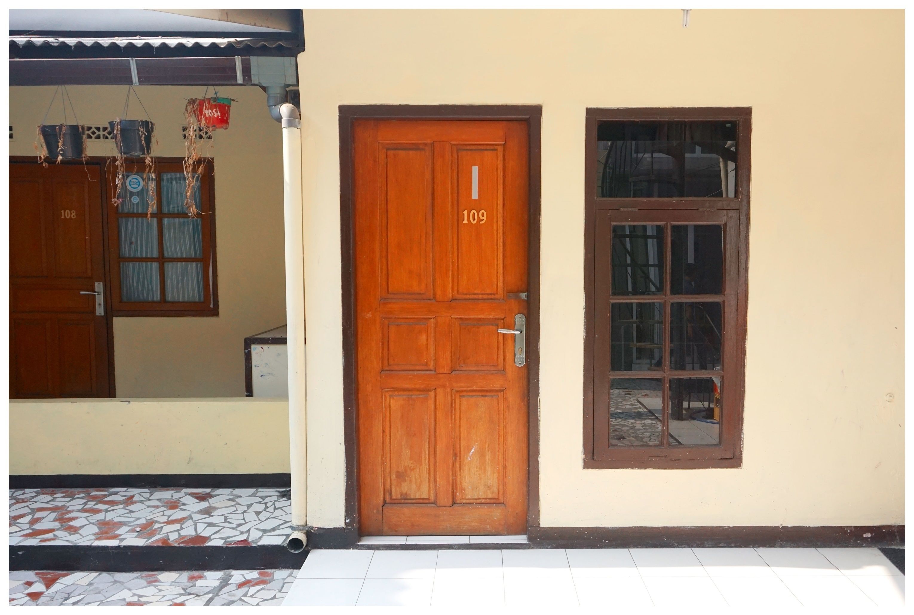 Una puerta de madera con el número 109, una ventana con diseño de cuadrícula y una zona de entrada con baldosas.