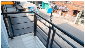 A balcony with a metal railing overlooking a street with shops and vehicles. - Budi House & Food Station (Cimahi)