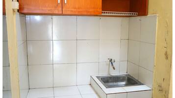 A kitchen with white tiled walls, a stainless steel sink, and wooden cabinets.