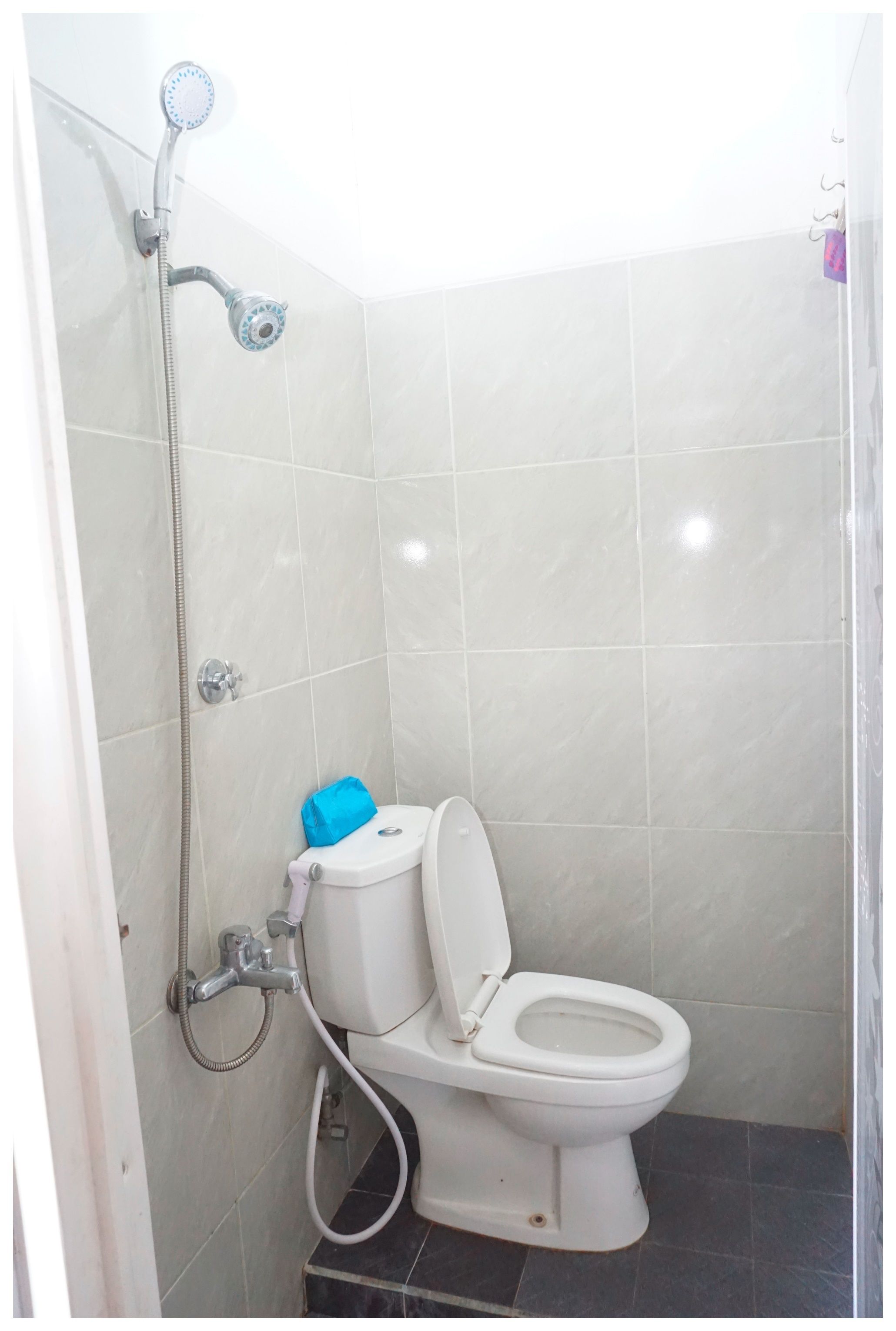 A small, enclosed bathroom with a toilet, a shower head, and a handheld shower attachment.