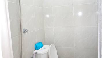 A small, enclosed bathroom with a toilet, a shower head, and a handheld shower attachment.