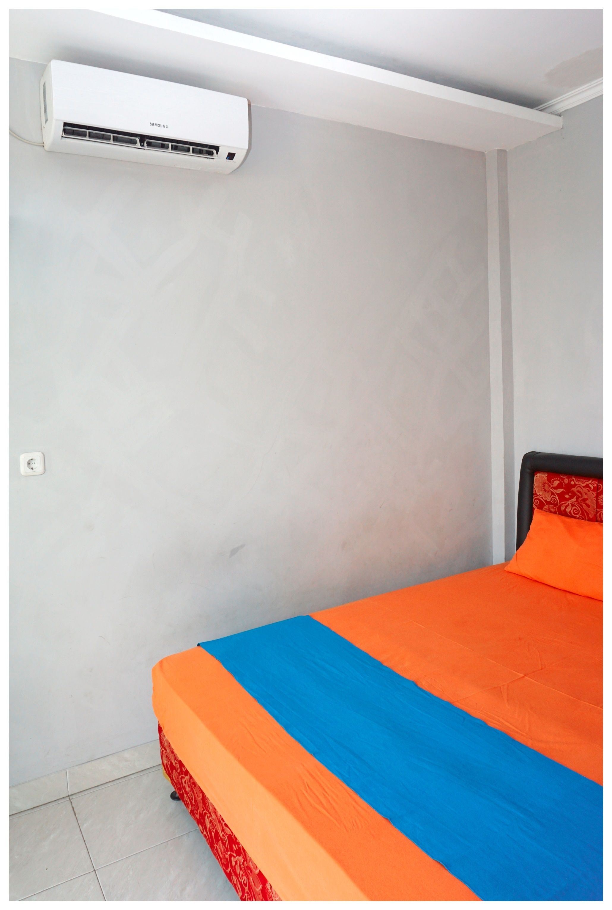 A room with a bed, an air conditioning unit, and a light switch on the wall.