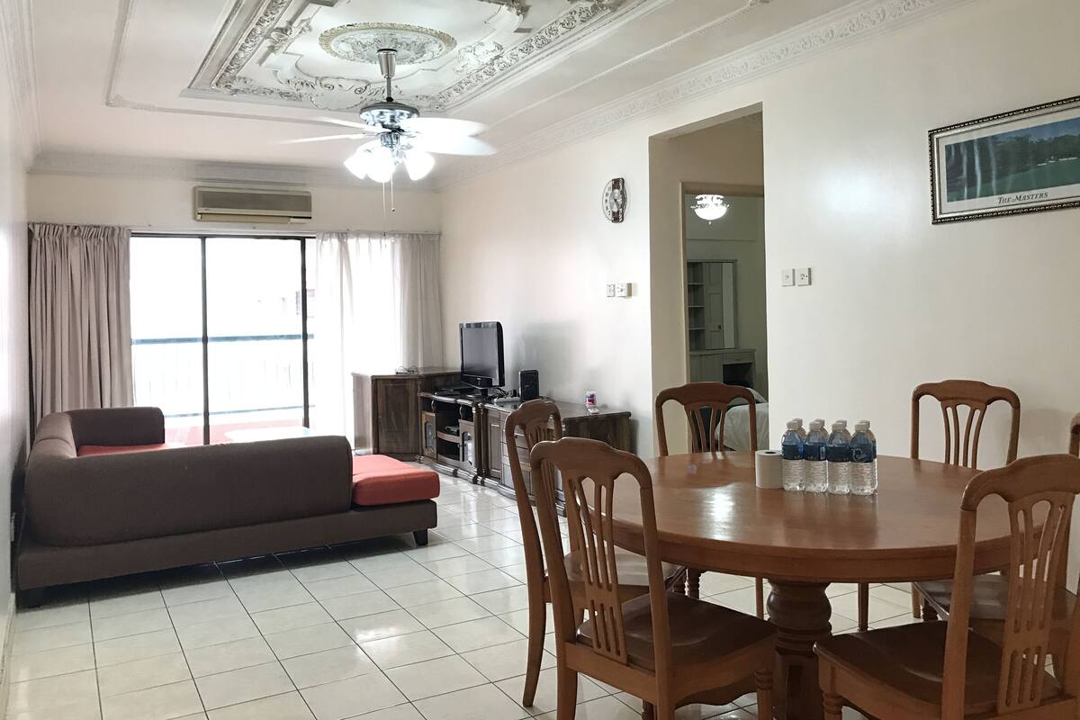 Una sala de estar con un sofá, una mesa de comedor con sillas, un televisor y un ventilador de techo.