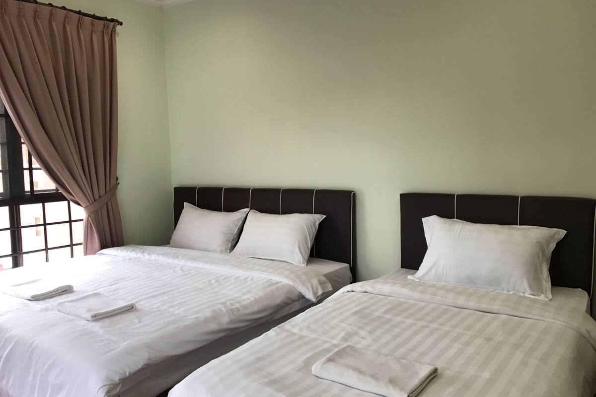 Dos camas individuales con sábanas y almohadas blancas, una ventana con cortinas y una pared lisa.