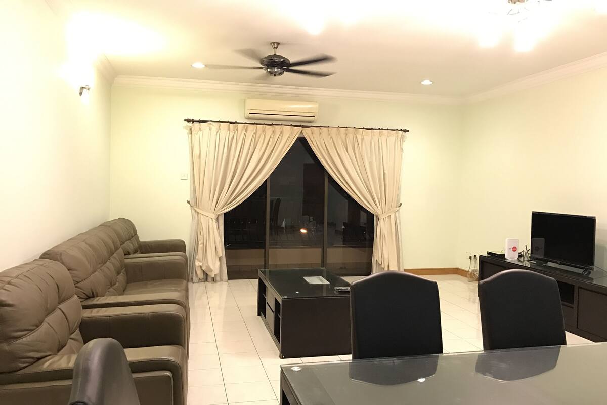 Una sala de estar con sofá, una mesa de comedor con sillas, televisor y aire acondicionado.