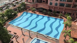 An aerial view of a swimming pool surrounded by a building with multiple balconies and a parking area with vehicles. - Sunset & Seaview Vacation Condos at Marina Court Resort Condo (Kota Kinabalu)