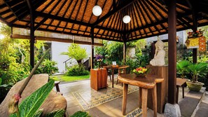 Un espacio al aire libre techado con mobiliario de madera, una estatua y plantas en macetas.