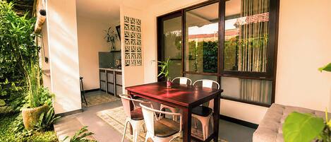 A dining area with a wooden table and chairs, a potted plant, and a view through a large window.