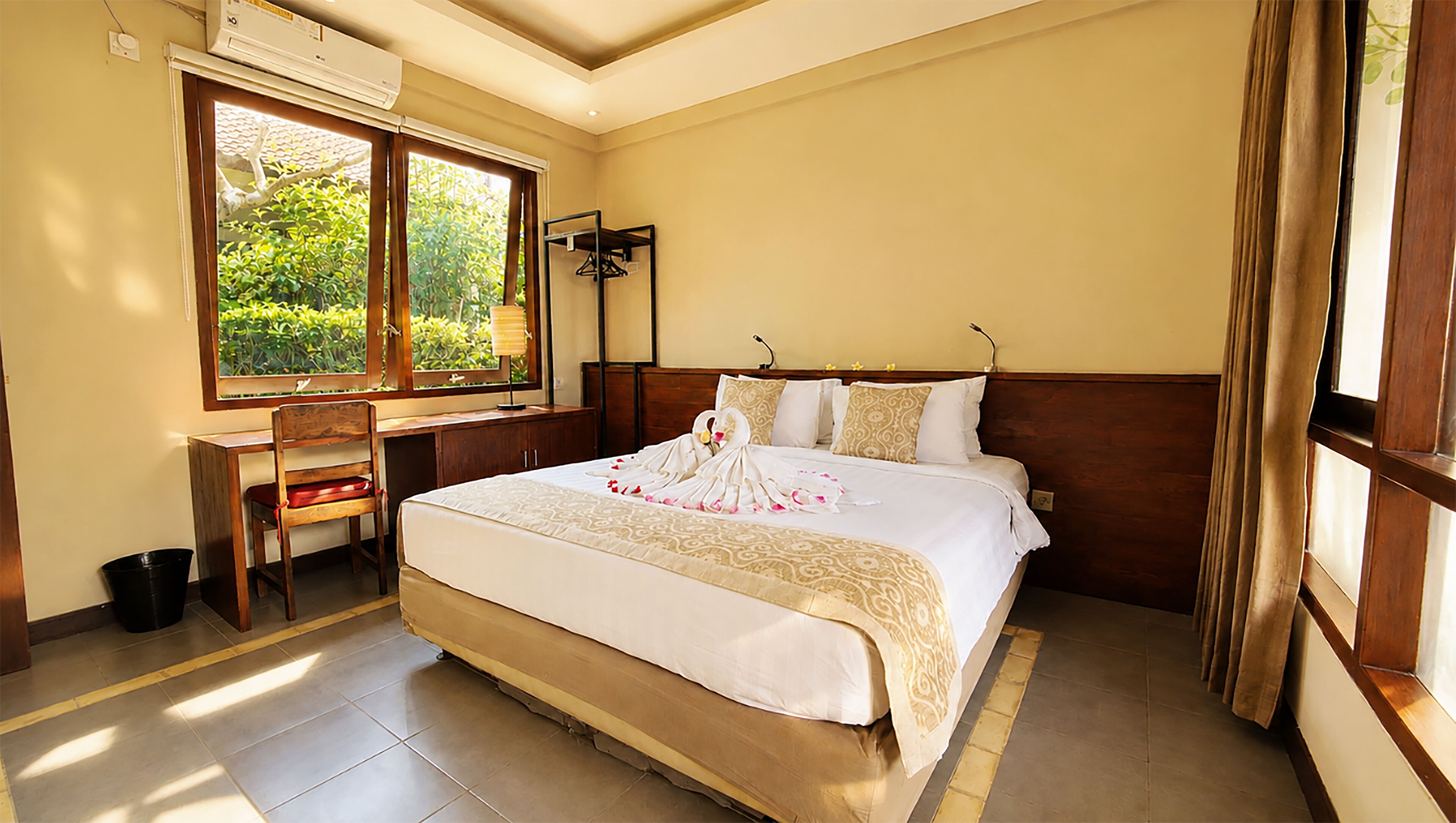 A hotel room with a large bed, a desk, and a window with a view of greenery.