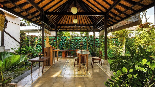 Un patio al aire libre con techo de paja, muebles de madera y exuberante vegetación tropical.