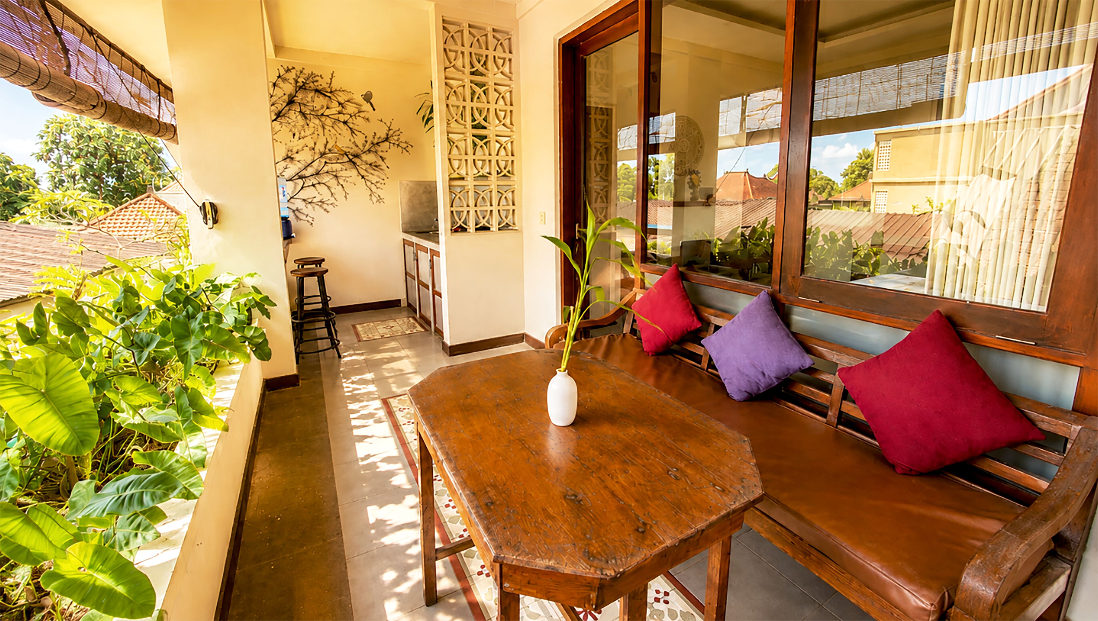 A wooden table with a vase, a bench with cushions, and a view of the outside.