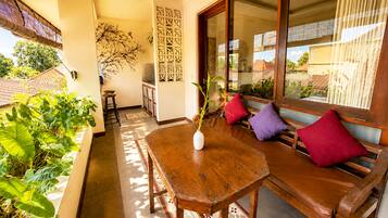 A wooden table with a vase, a bench with cushions, and a view of the outside.