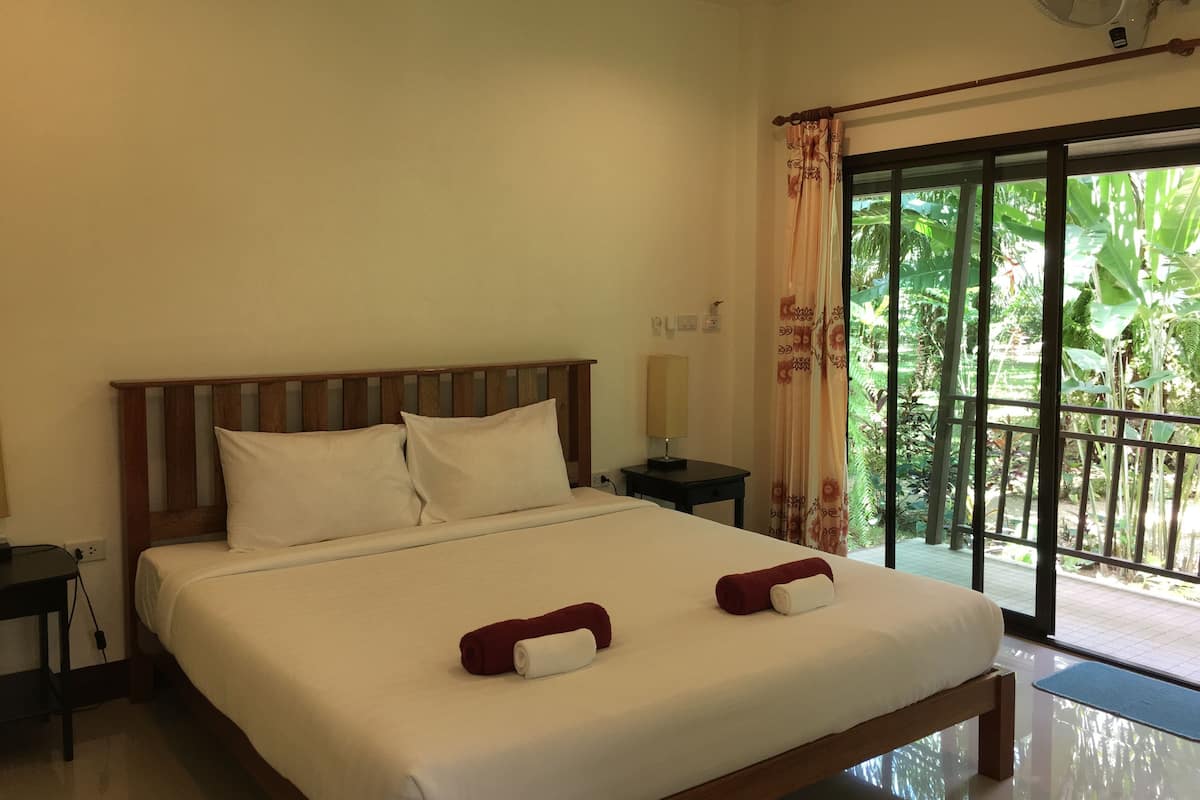 A hotel room with a large bed, a bedside table, a lamp, and a view of greenery through the window.