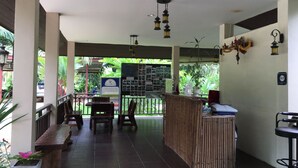 A covered outdoor seating area with wooden benches and tables, a reception desk, and hanging lanterns. - Khao Sok Palm Garden Resort (Phanom)
