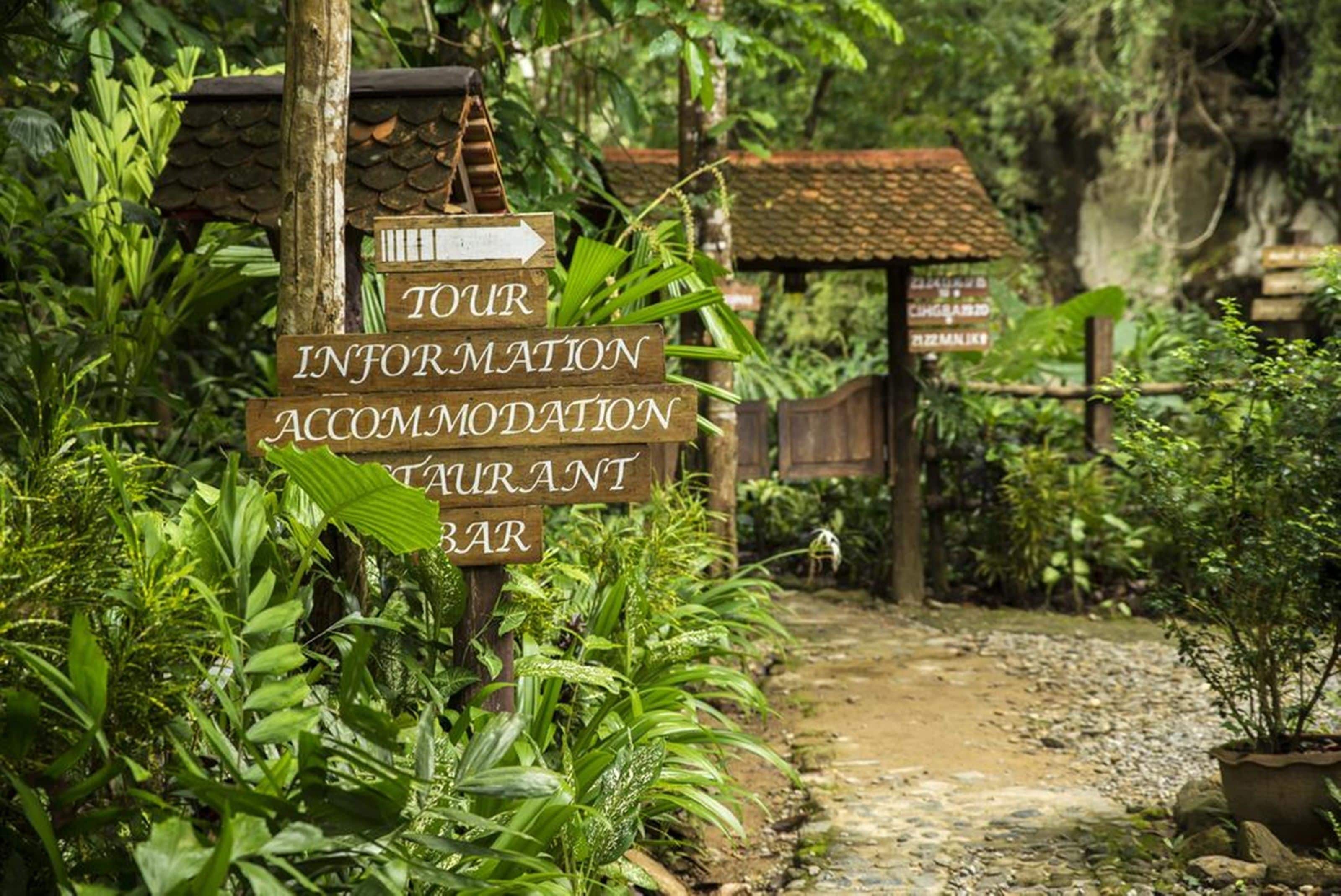 A rustic wooden signpost with directions to a tour information center, accommodation, and restaurant/bar.