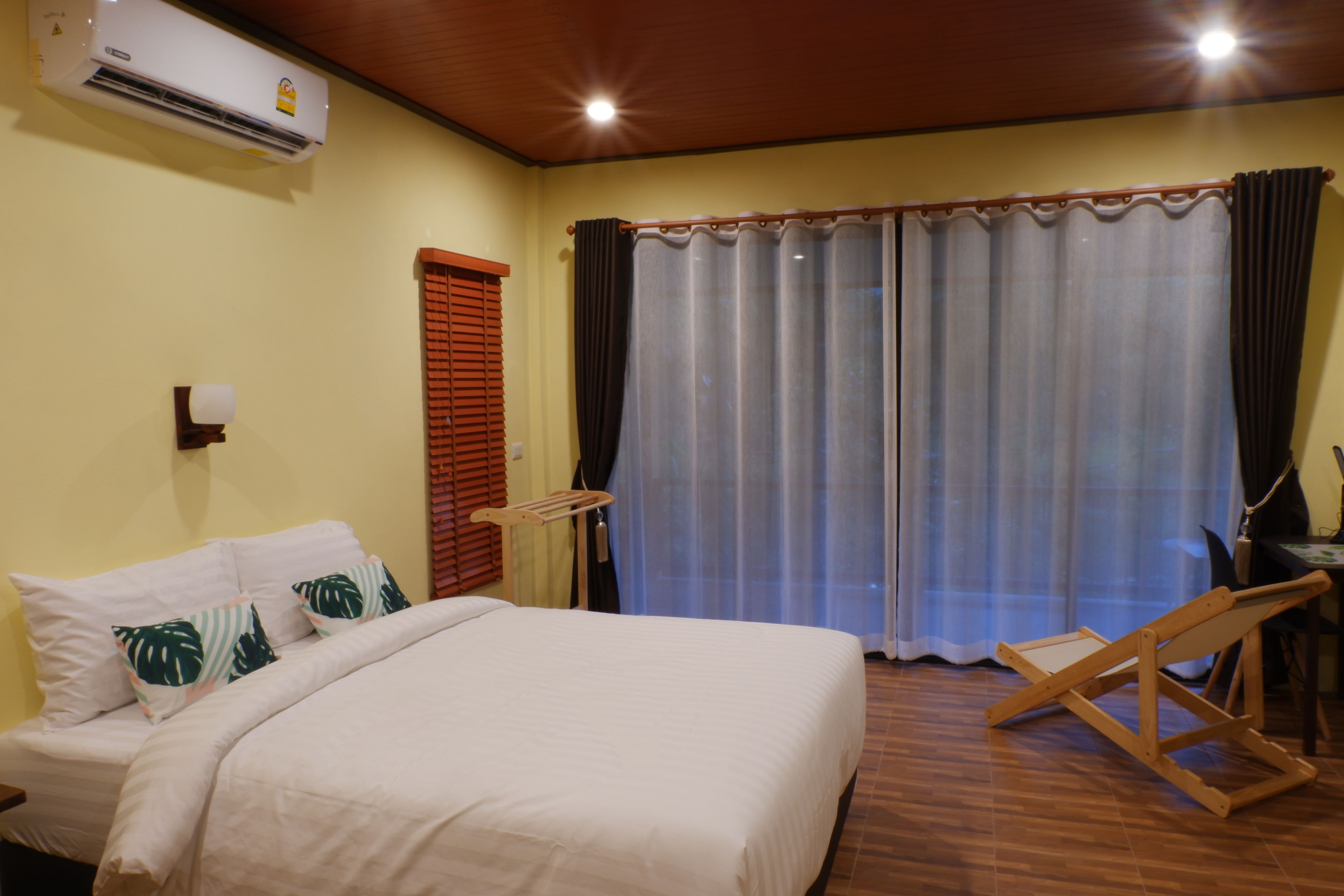 Een hotelkamer met een bed, een airconditioner, een houten bankje en een raam met gordijnen.
