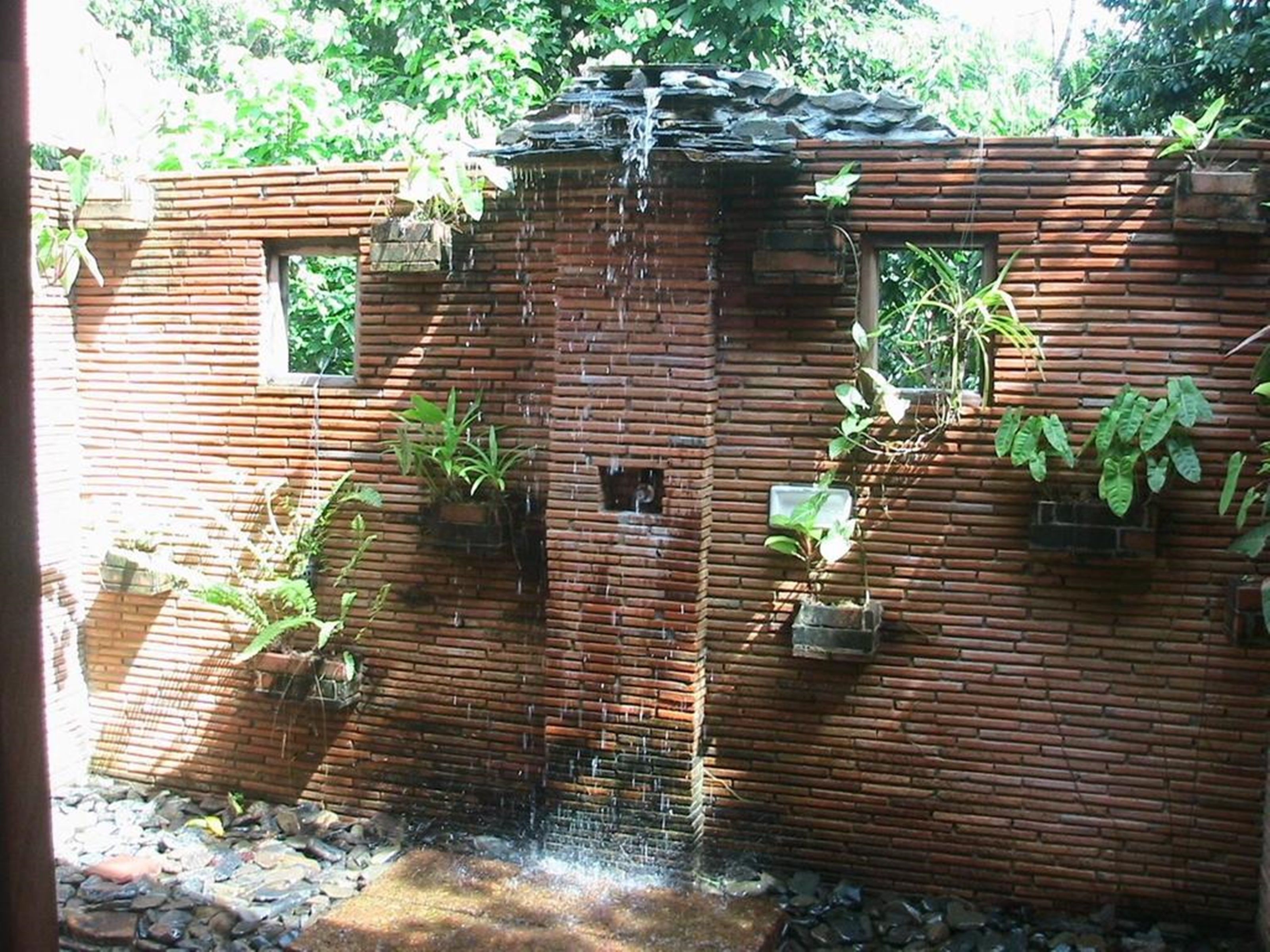 A rustic brick building with a small waterfall feature, potted plants, and a window.