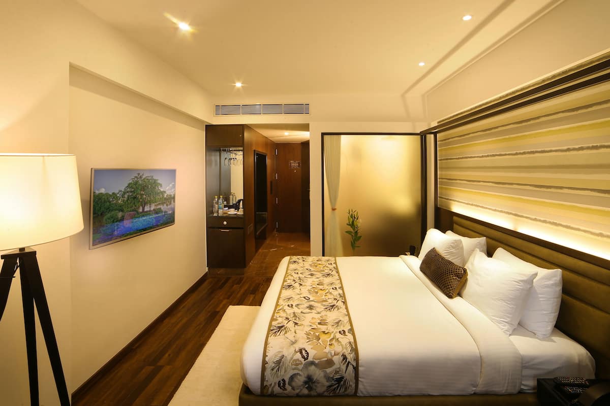 Habitación de hotel con una cama grande, un escritorio con lámpara, un cuadro en la pared y vistas al pasillo.