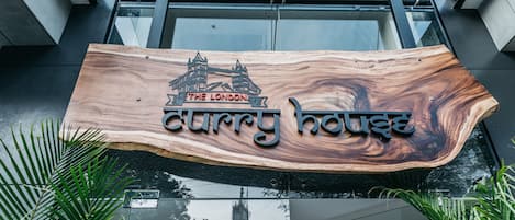 A wooden sign with a bridge and the text "The London Curry House" above a modern building entrance.