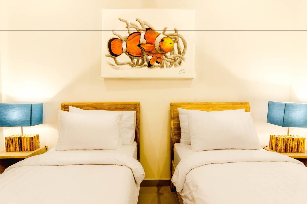 A hotel room with two beds, wooden headboards, white bedding, and a painting of fish on the wall.