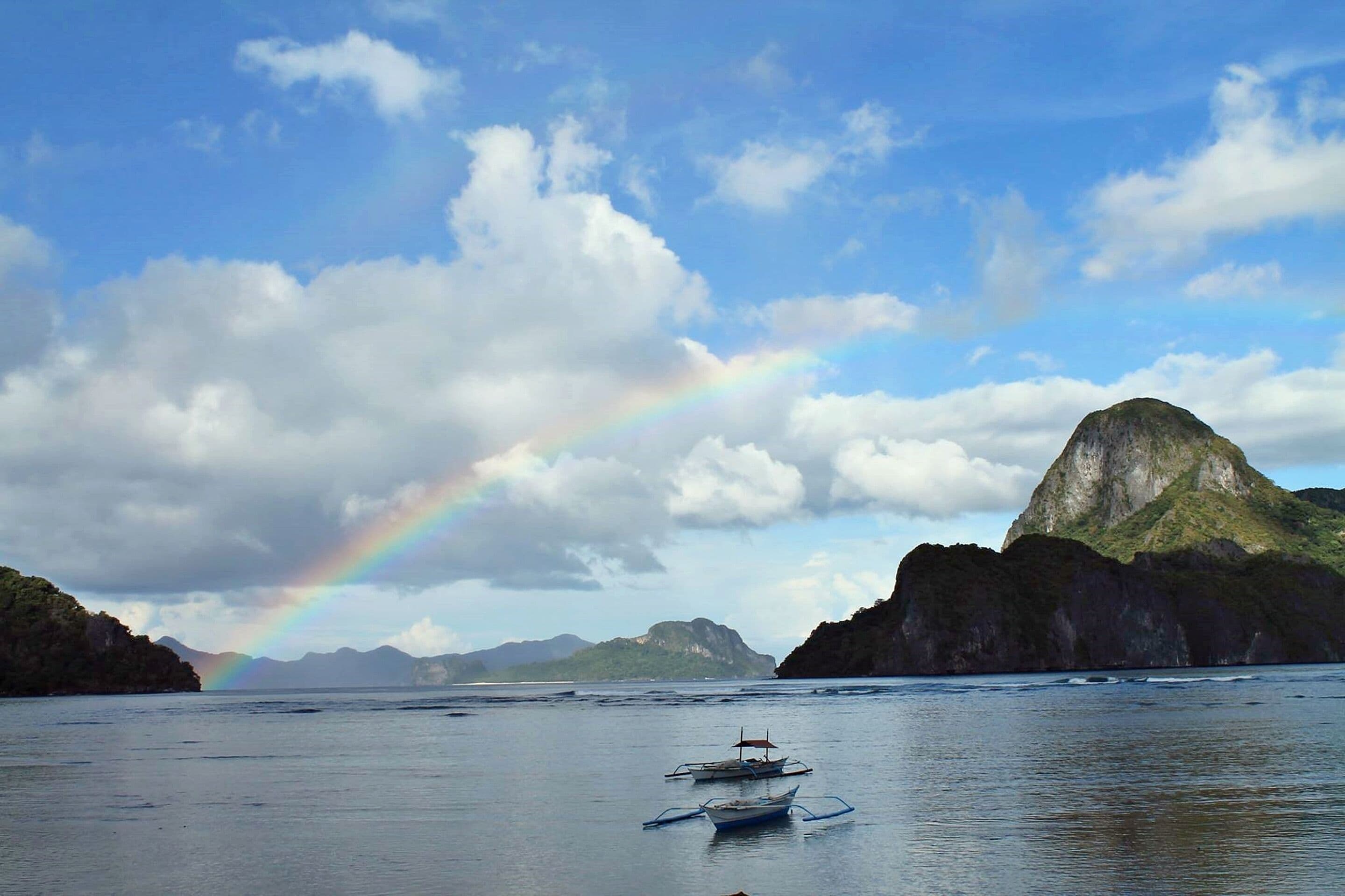 A coastal scene with boats, a mountain, and a rainbow.