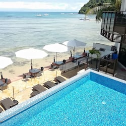 Relax by the pool, surrounded by lounge chairs and umbrellas, with the sea and boats in view.