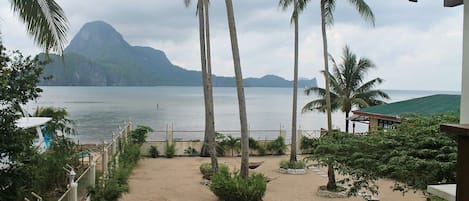 Une plage avec des palmiers, un sentier sablonneux et une montagne en arrière-plan.
