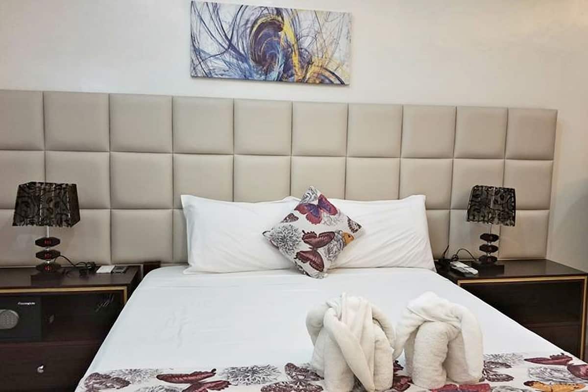 A hotel room with a large bed, two bedside lamps, a green armchair, and a painting on the wall.