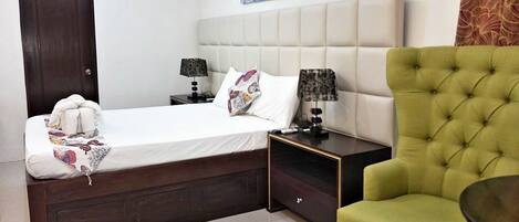 A hotel room with a bed, two bedside tables, a green armchair, and a painting on the wall.