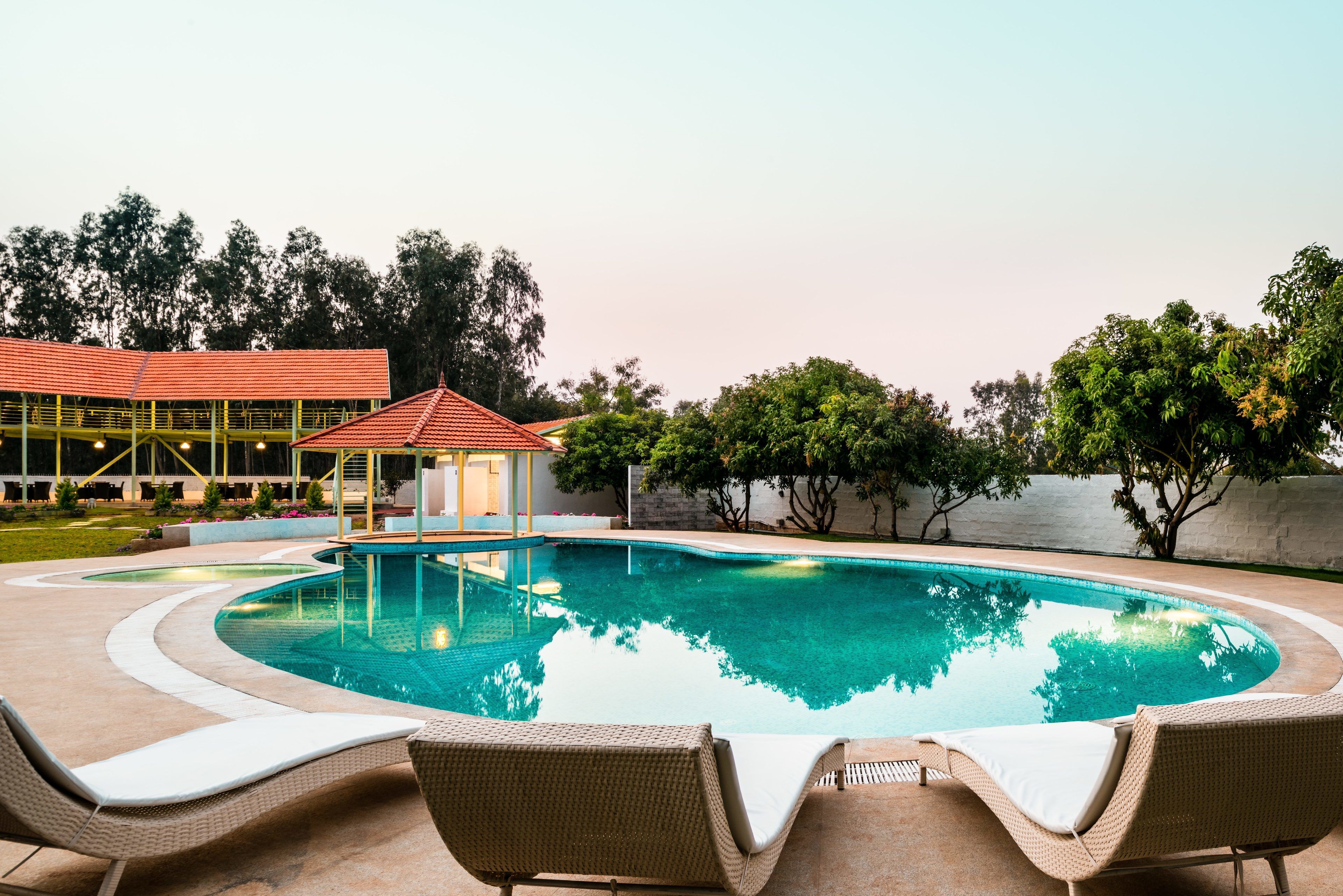A swimming pool with lounge chairs, a gazebo, and a building with a red roof in the background.