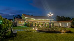 A modern house with a well-lit garden, a covered patio, and a pool. - Fiestaa Resort n Events Venue (Bengaluru)