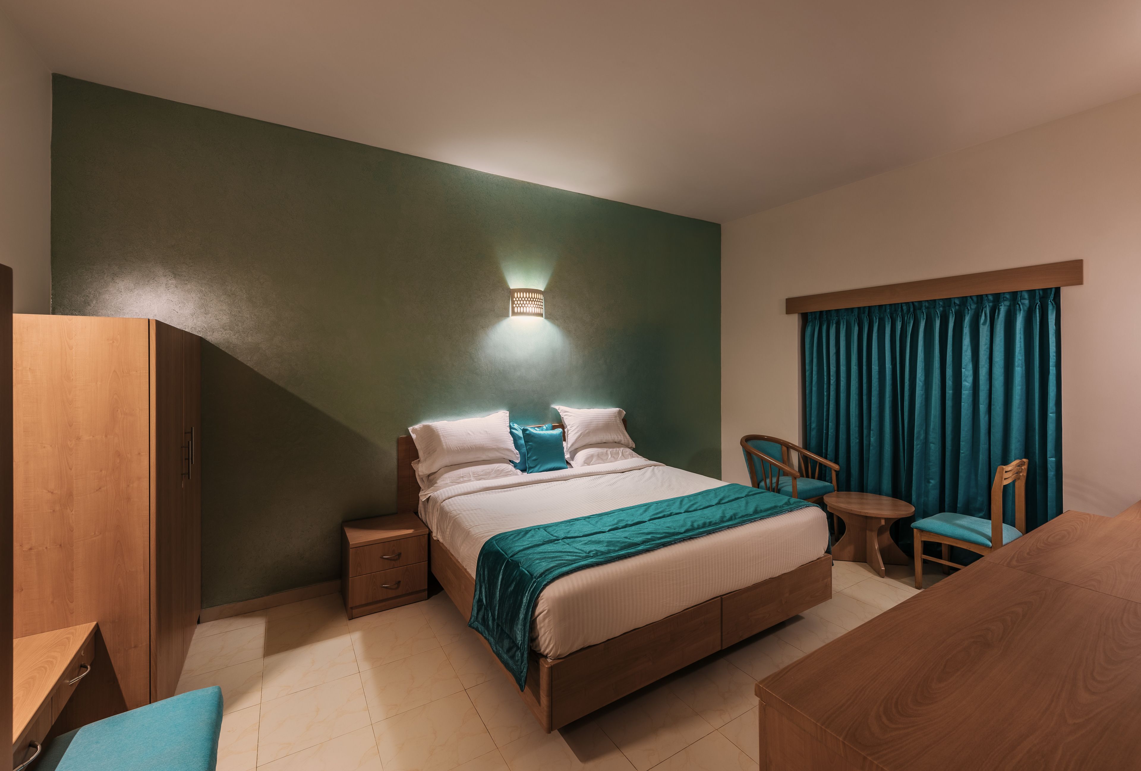 A hotel room with a bed, bedside tables, a desk, a chair, and a window with curtains.