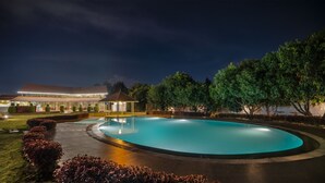 A nighttime swimming pool area with a gazebo, well-maintained lawn, and a building with a tiled roof. - Fiestaa Resort n Events Venue (Bengaluru)