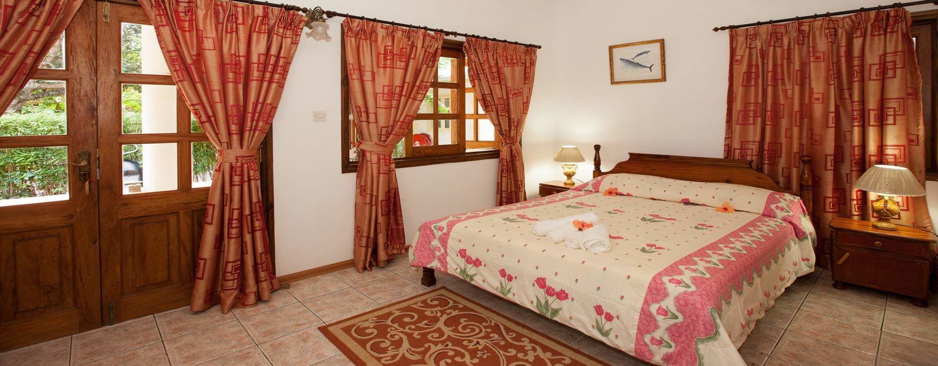 Un dormitorio con cama, cortinas, mesita de noche, lámpara y ventana.