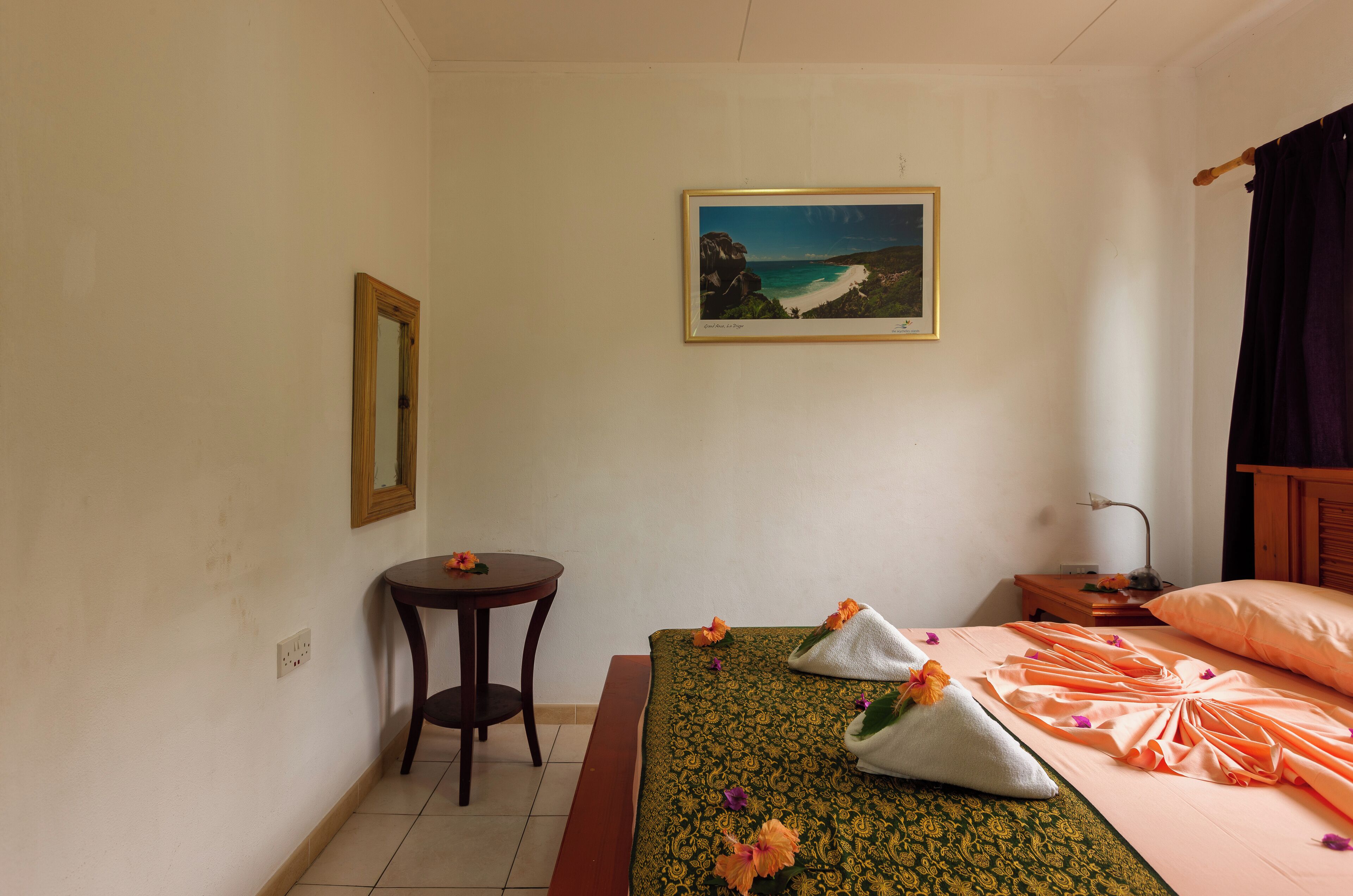 Une chambre d’hôtel bien rangée, avec un lit, une petite table ronde, une table de chevet et un tableau encadré au mur.