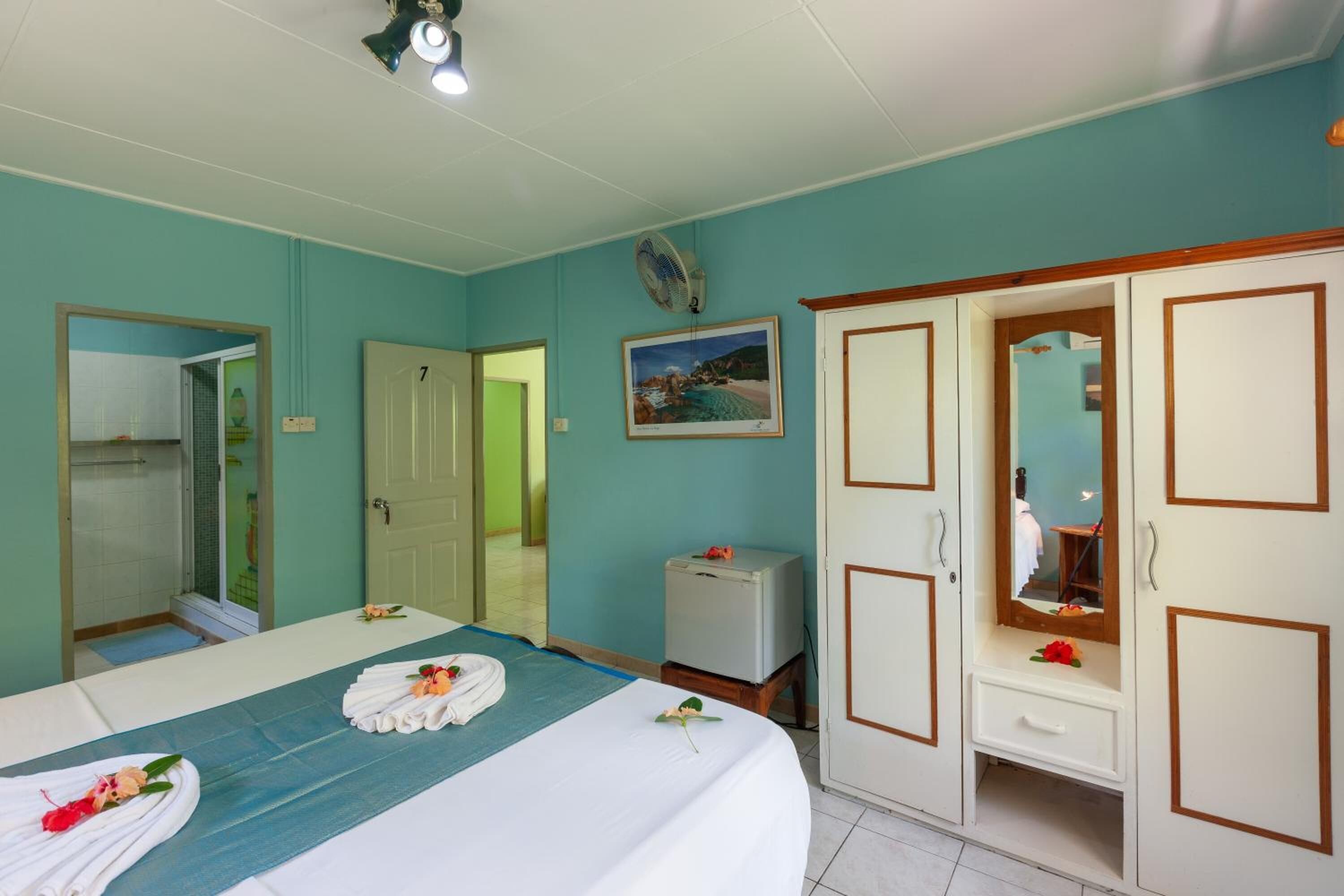 Habitación de hotel con cama, armario, espejo, una mesita y un cuadro en la pared.