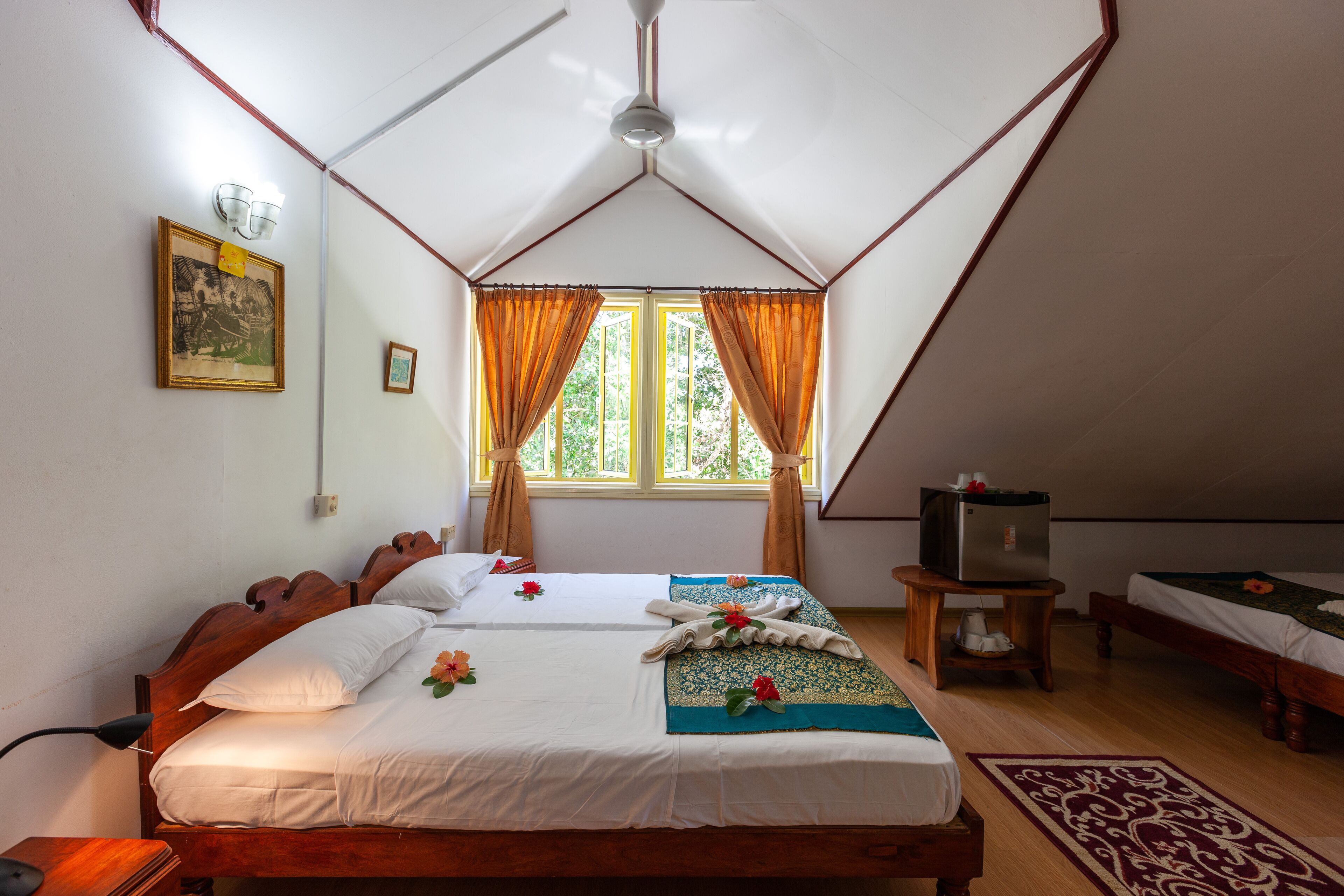 A bedroom with two beds, a ceiling fan, a television on a side table, and a window with curtains.