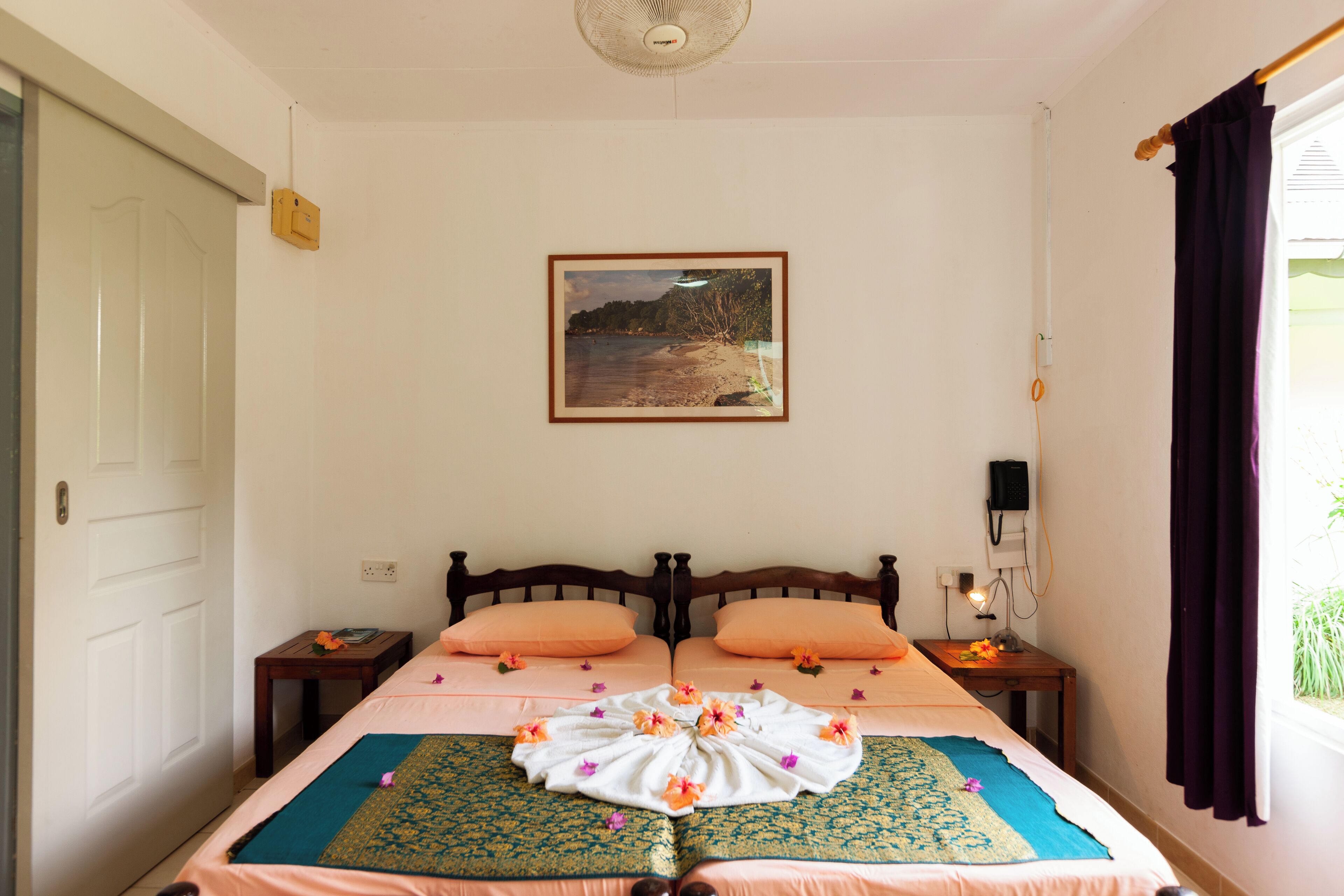 A bedroom with a bed, a bedside table, a nightstand, a wall-mounted picture, and a window with curtains.