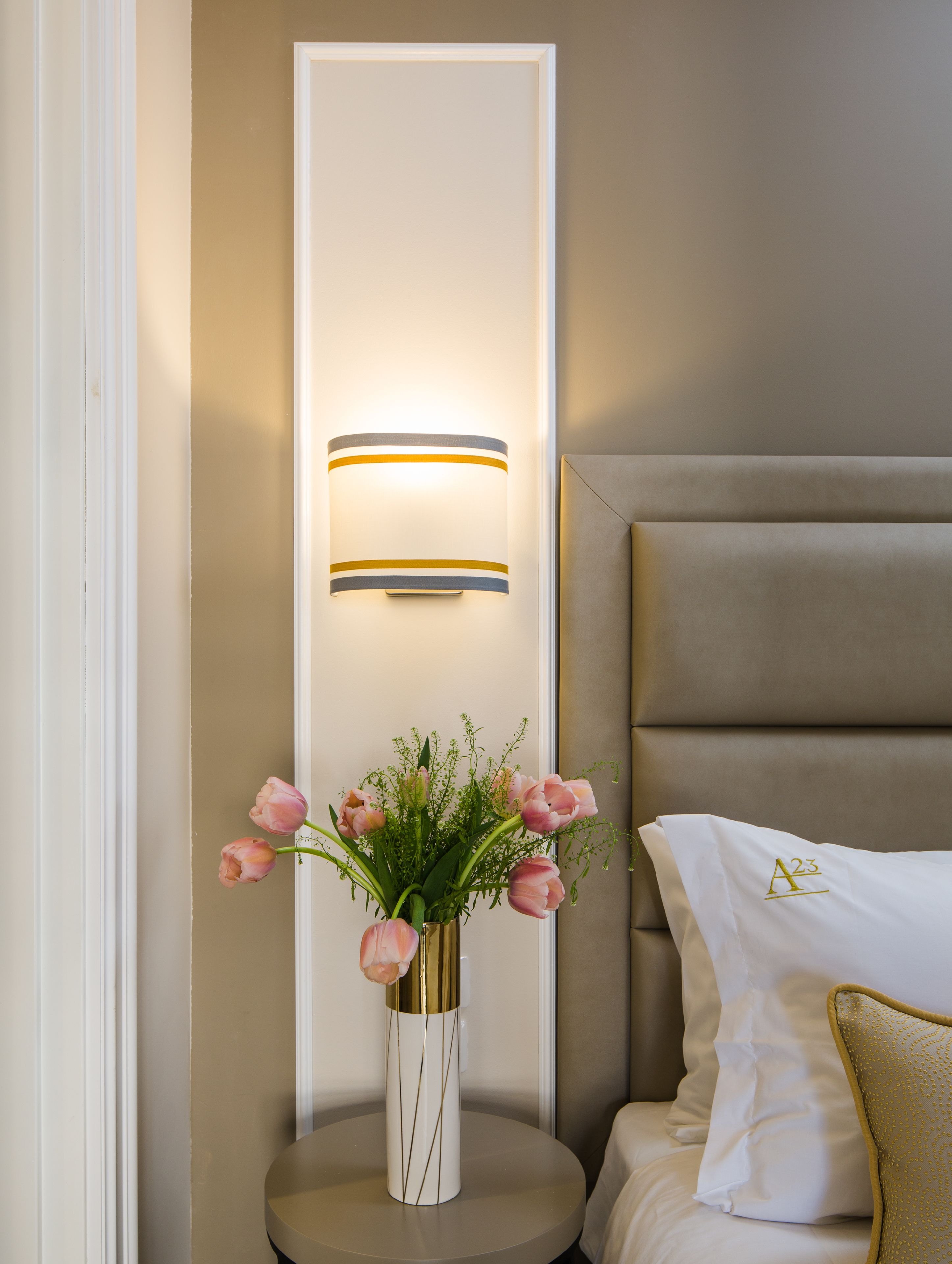 A bedroom with a bed, a bedside table with a vase of flowers, and wall-mounted lighting.