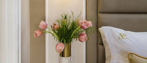 A bedroom with a bed, a bedside table with a vase of flowers, and wall-mounted lighting.